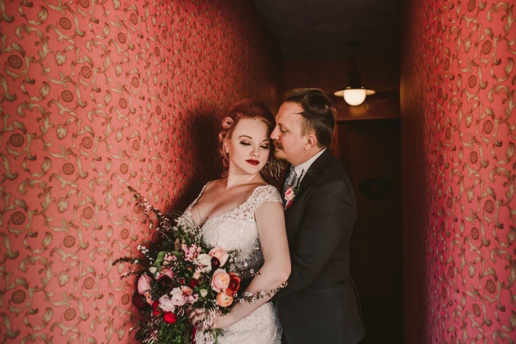 Husband hugging bride in a pink wallpaper hallway